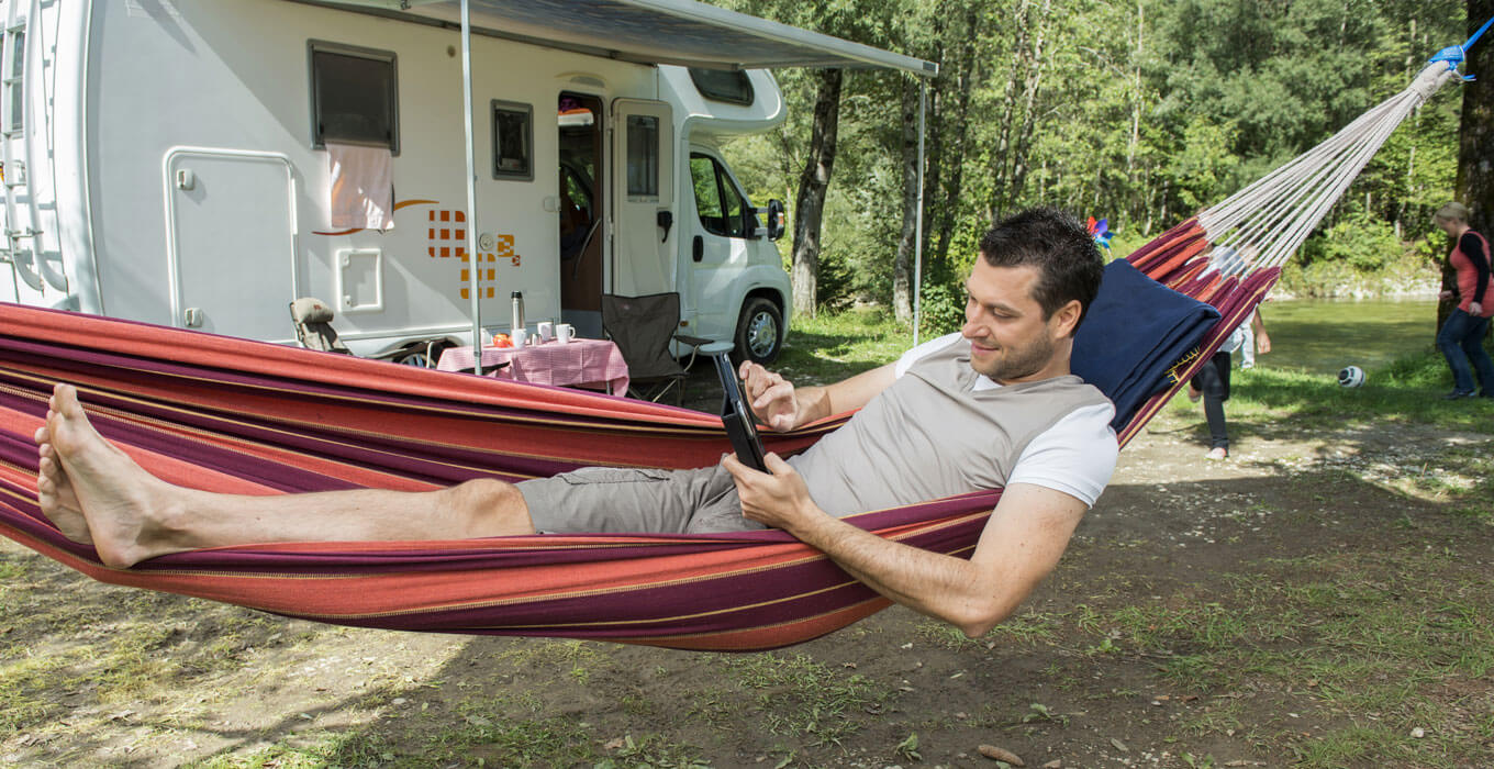 Man laying in hammock at a campsite looking at tablet
